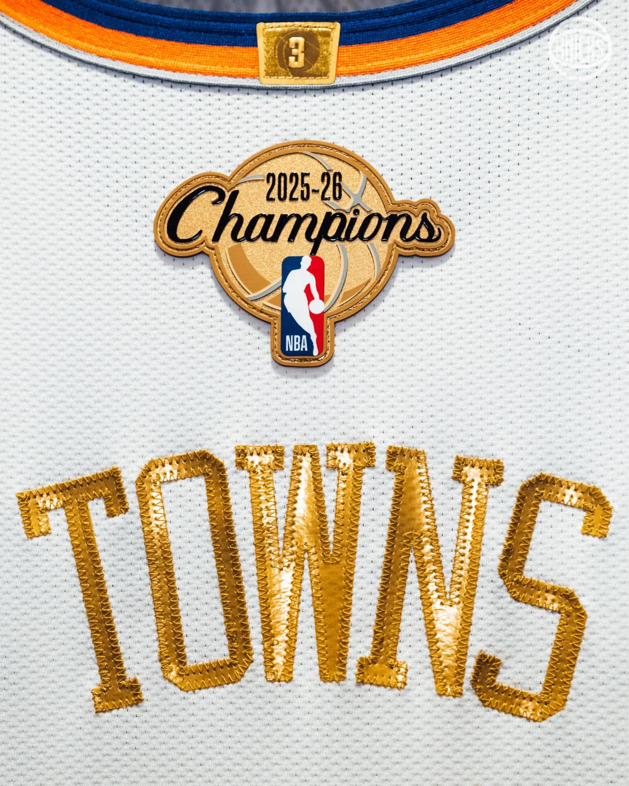 Back of the Knicks ring night jersey: gold 2025-26 Champions patch with the NBA logo above a metallic gold TOWNS nameplate on white mesh, with a gold 3 tag at the orange and blue collar