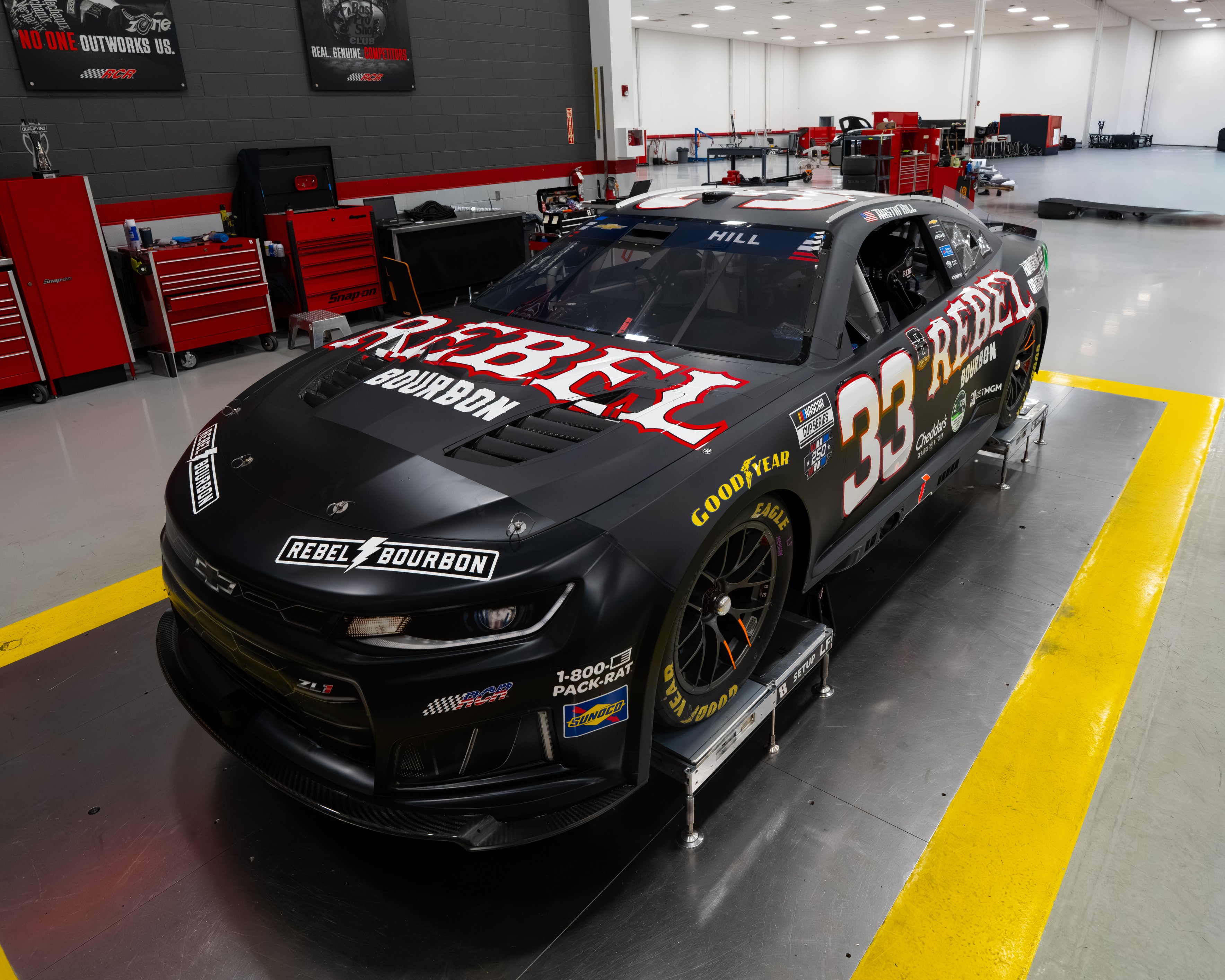 Austin Hill's #33 Richard Childress Racing Chevrolet for the 2026 NASCAR Cup Series in matte black with red REBEL BOURBON wordmark across the hood and quarter panels, the Rebel Bourbon Kyle Busch tribute paint scheme revealed at the RCR shop
