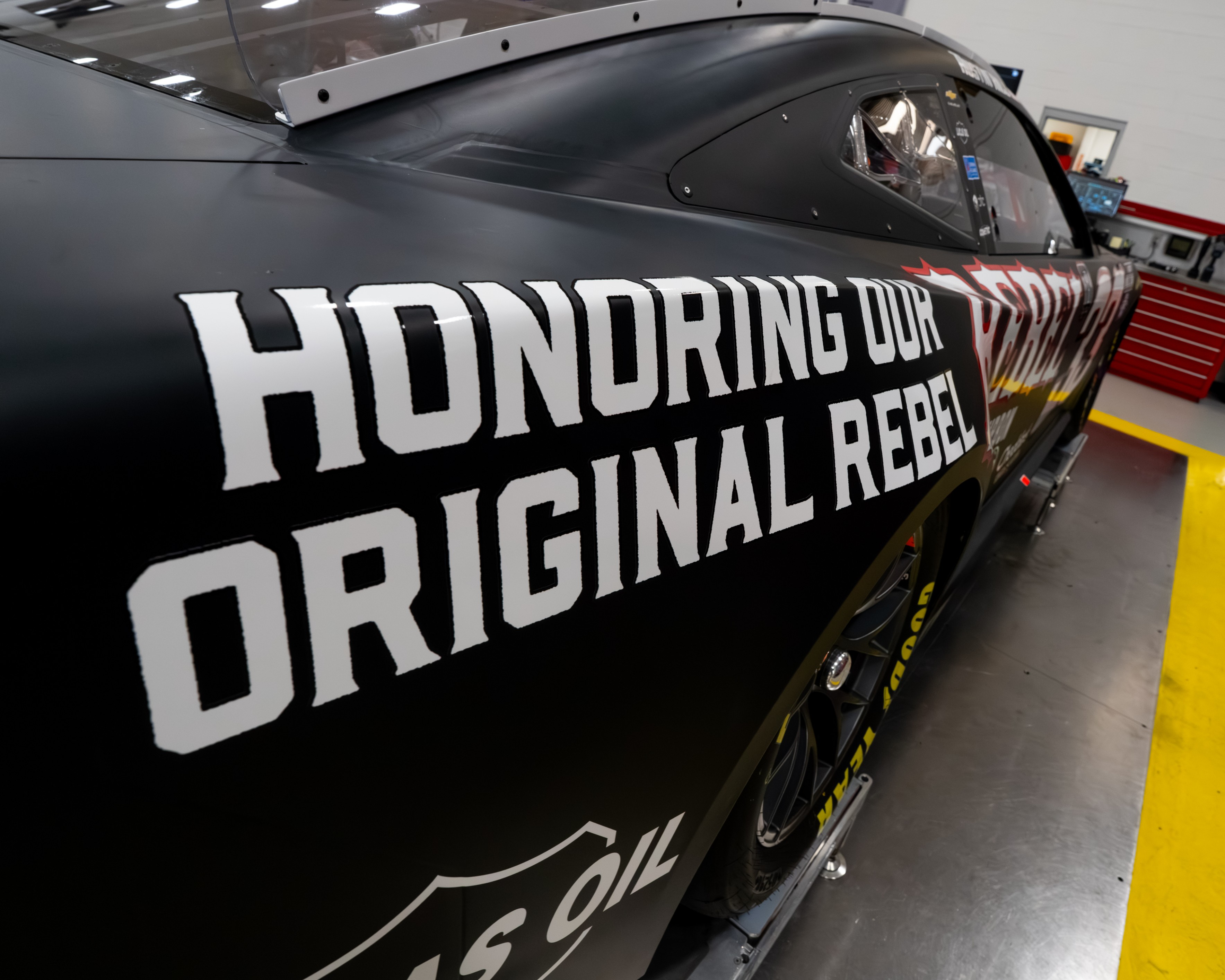 HONORING OUR ORIGINAL REBEL text on the matte black quarter panel of Austin Hill's new #33 Richard Childress Racing Chevrolet for the 2026 NASCAR Cup Series, the Rebel Bourbon Kyle Busch tribute paint scheme revealed at the RCR shop in Welcome North Carolina