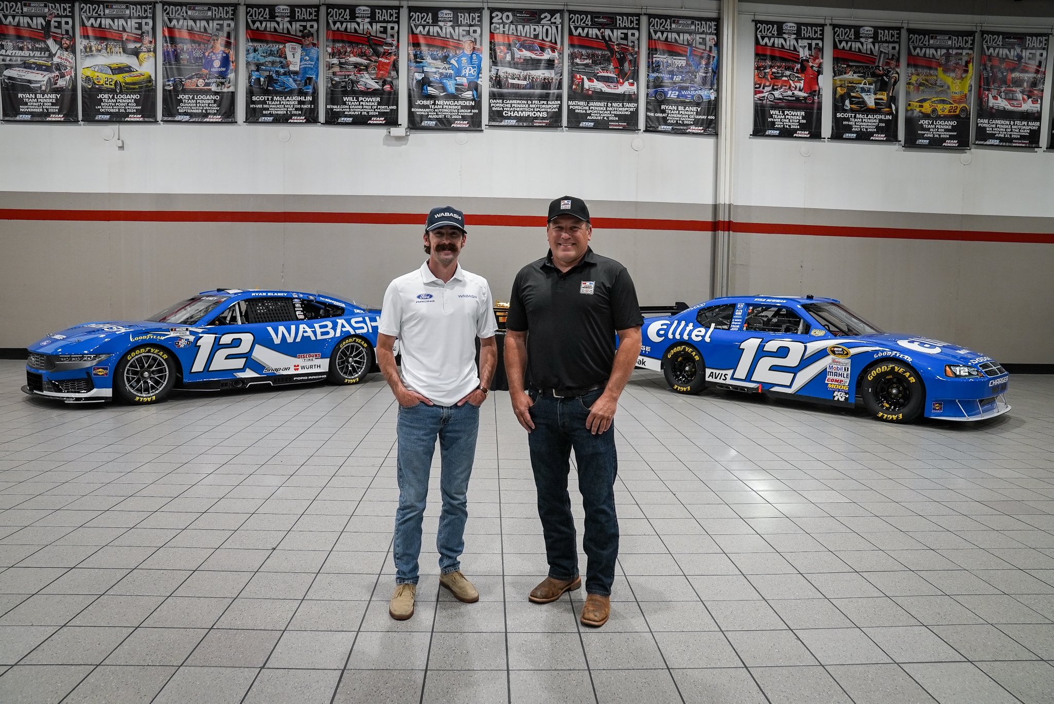 Ryan Blaney and Ryan Newman standing together inside the Team Penske shop between the 2026 number 12 Wabash throwback Ford Mustang Dark Horse and Ryan Newman's original royal blue Alltel number 12 Dodge from the 2008 Daytona 500 win, with 2024 race winner posters lining the wall above them