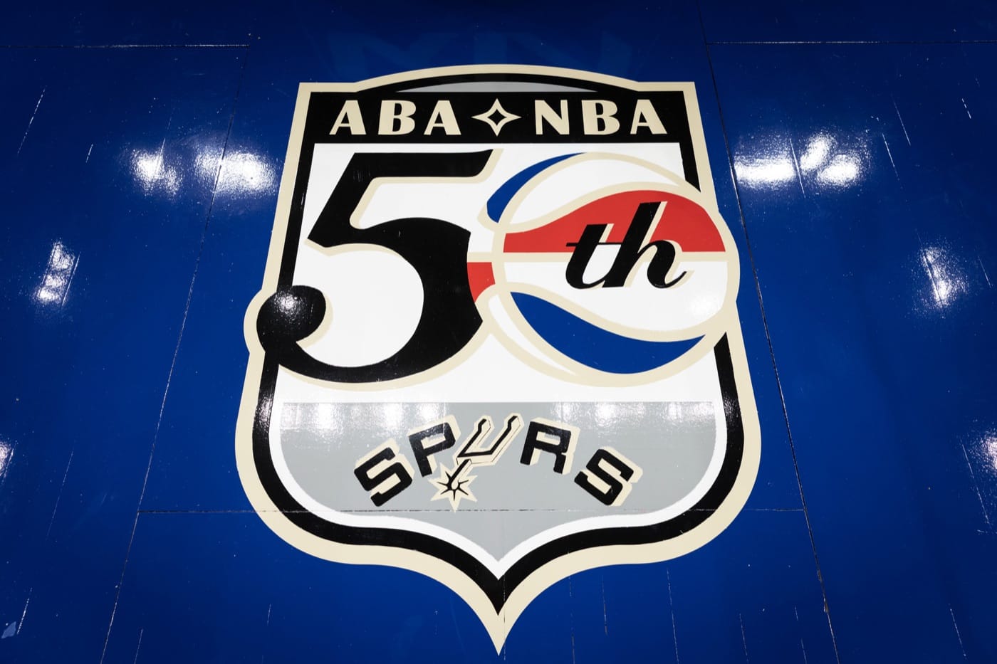 ABA-NBA 50th anniversary logo with the Spurs wordmark, painted on the blue apron of the San Antonio Spurs 2026-27 Classic Edition court