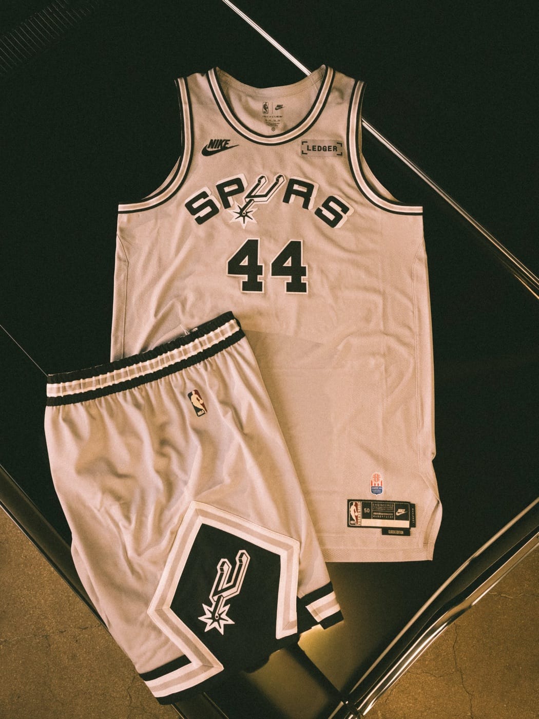 San Antonio Spurs 2026-27 Classic Edition uniform laid flat: silver jersey with the arched SPURS wordmark and No. 44, and shorts with the black diamond and spur logo