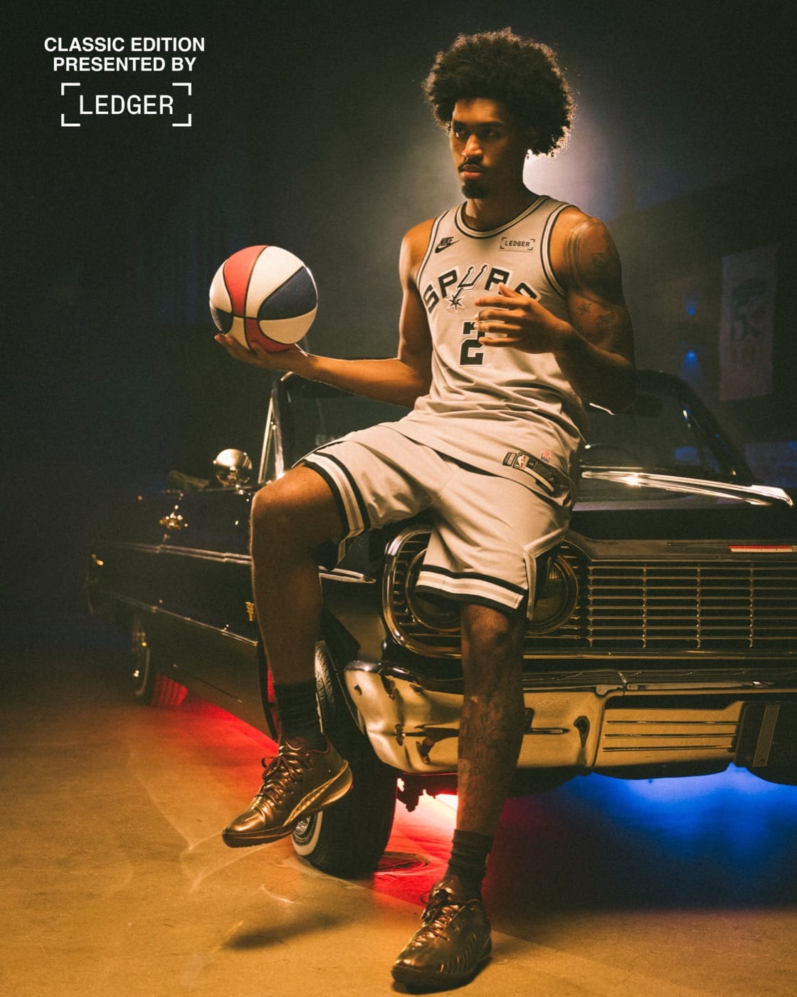 Spurs player in the silver 2026-27 Classic Edition jersey and shorts, holding a red, white and blue ABA ball