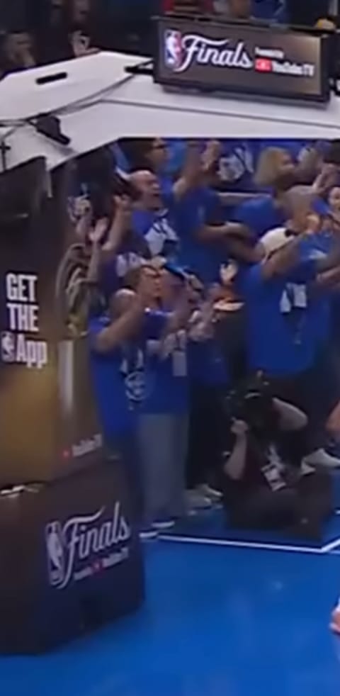 2025 NBA Finals stanchion showing the full NBA Finals wordmark and logo treatment on the base with crowd in blue t-shirts visible behind confirming the league still ran branded stanchion for the Finals even after stripping it from the earlier rounds