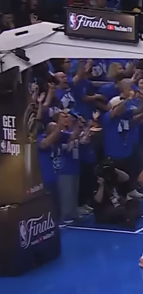 2025 NBA Finals stanchion showing the full NBA Finals wordmark and logo treatment on the base with crowd in blue t-shirts visible behind confirming the league still ran branded stanchion for the Finals even after stripping it from the earlier rounds