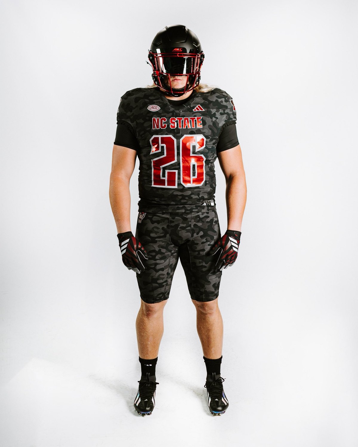 NC State Wolfpack Warriors uniform, a dark camouflage jersey and pants with red NC STATE lettering, large red numbers outlined in white, and a black helmet with a red facemask