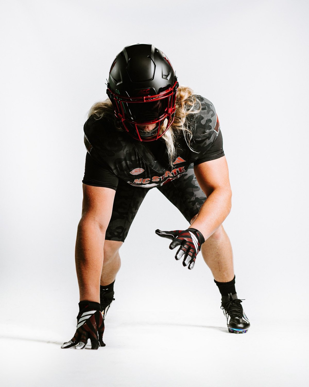 NC State Wolfpack Warriors camo uniform shown in a three point stance, showing the camo pattern across the jersey and pants