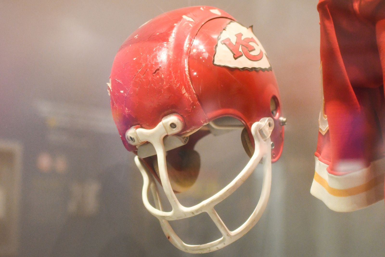 A worn red Kansas City Chiefs helmet with the white arrowhead and red interlocking KC logo, on display at the Pro Football Hall of Fame