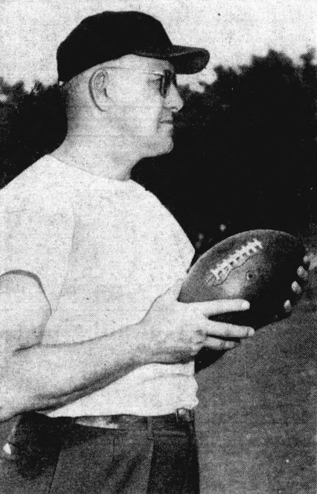 Black and white photo of Bears founder and coach George Halas in a cap and sweatshirt, holding a football, in 1950