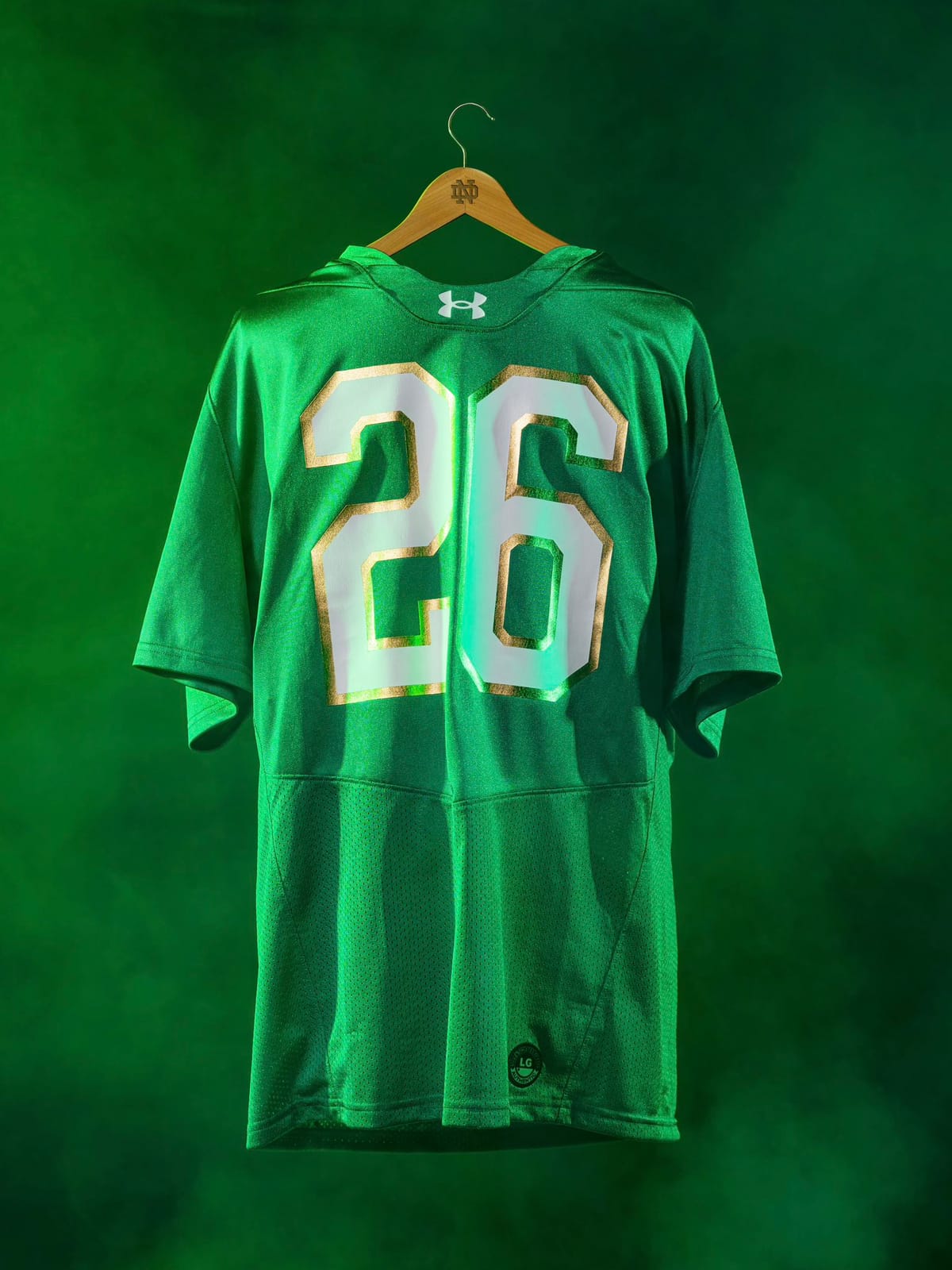 Full view of the Notre Dame 2026 Irish Wear Green replica jersey on a Notre Dame hanger against a green backdrop