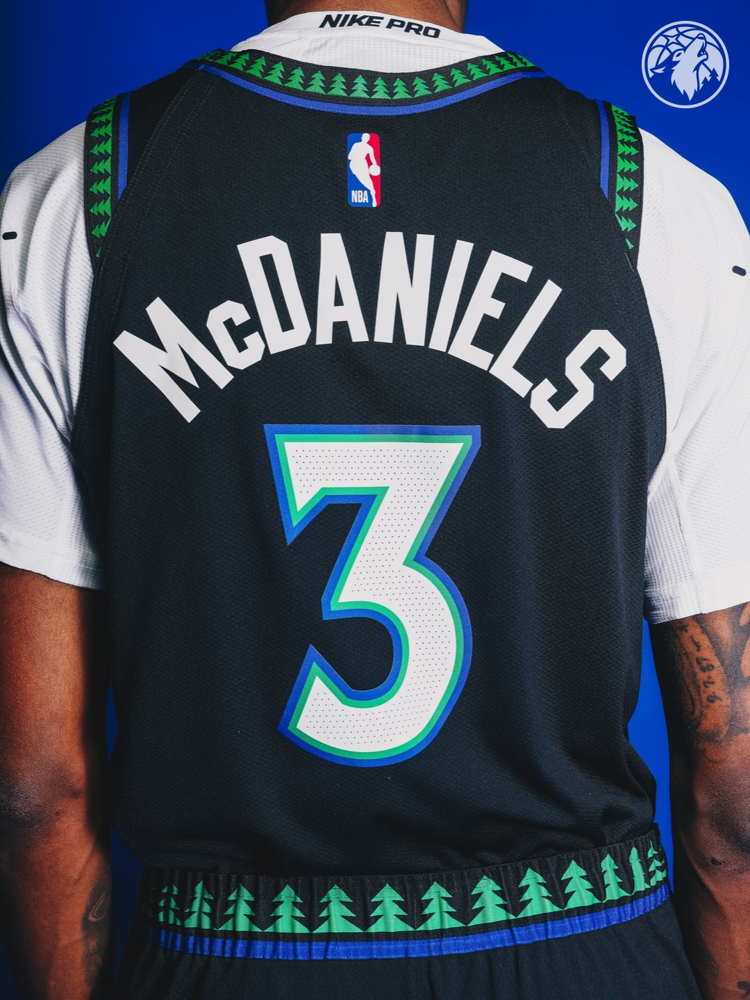 Minnesota Timberwolves new Statement Edition black alternate jersey 2026-27 back view close-up of Jaden McDaniels number 3 with the white McDANIELS nameplate, the #3 in white with green and blue outline, the green tree print pattern running across the back yoke and the shorts waistband, the signature Hardwood Classic design element returning as the defining detail of the Wolves Statement Edition