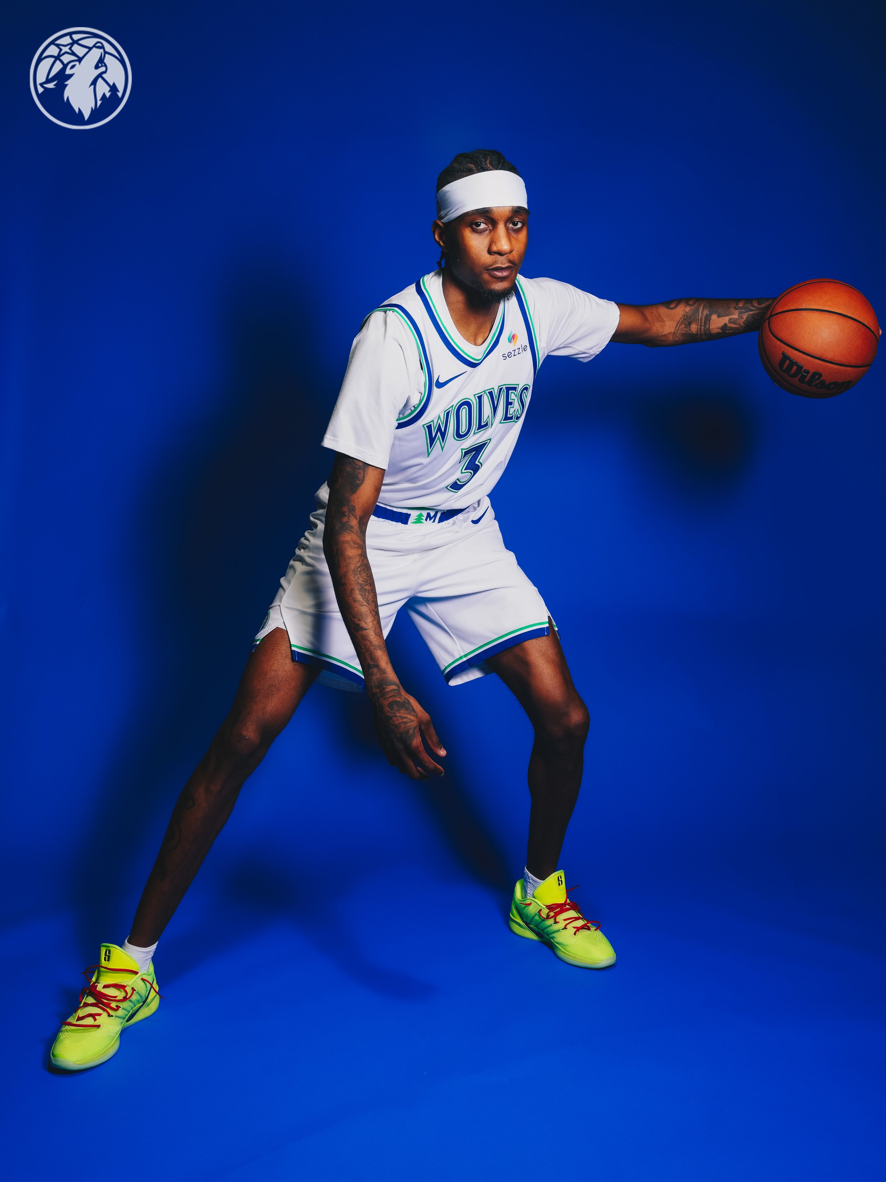 Minnesota Timberwolves new Association Edition white home jersey 2026-27 dribbling pose showing the full uniform in motion with the WOLVES throwback wordmark, the matching white shorts with green and blue trim, and the cut-out hem detail returning on the side of the shorts