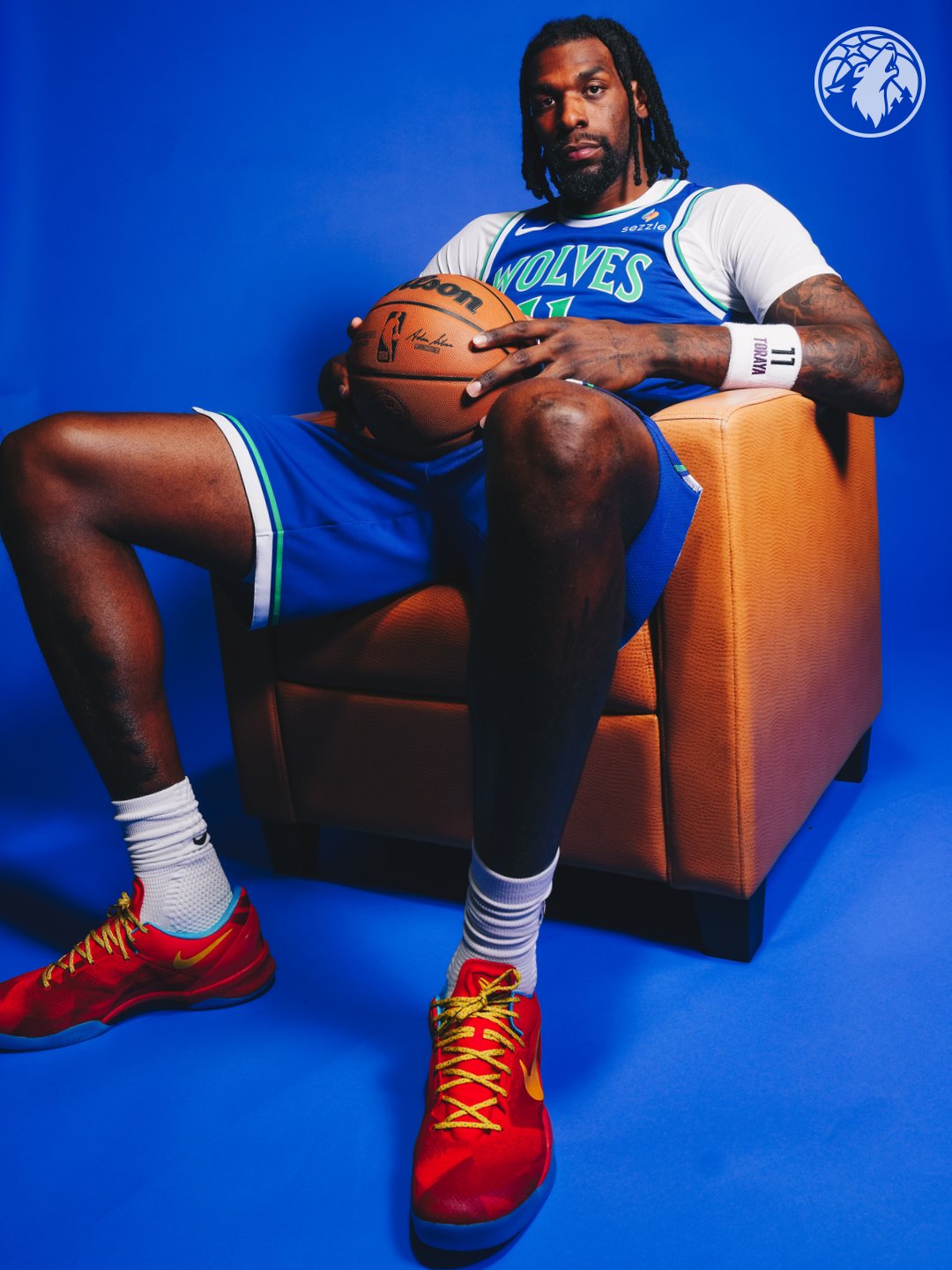Minnesota Timberwolves new Icon Edition blue road jersey 2026-27 full body seated pose on Naz Reid showing the throwback brighter blue base, the WOLVES green wordmark, the matching blue shorts with the green and white piping, and the green Torayan number eleven wristband detail