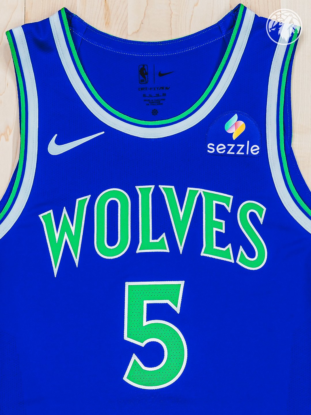 Minnesota Timberwolves new Icon Edition blue road jersey 2026-27 laid flat product shot showing the front view with the WOLVES wordmark in bright green with green outline, the #5 chest number for Anthony Edwards in green numerals, the saturated brighter blue base, and the Sezzle jersey patch on the right chest