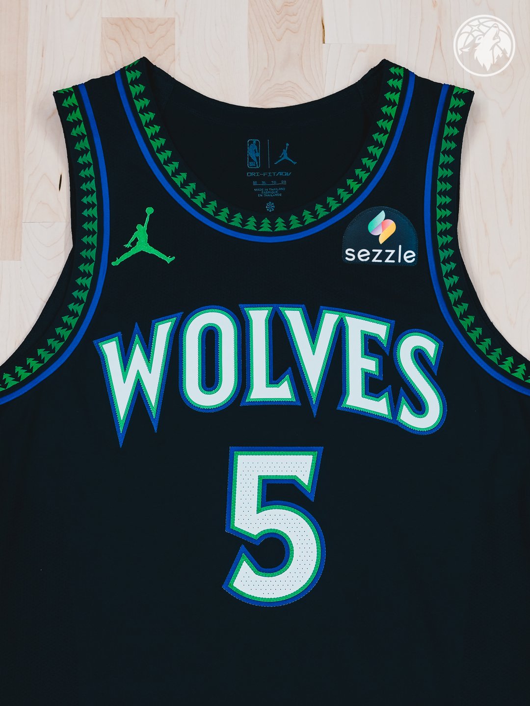 Minnesota Timberwolves new Statement Edition black alternate jersey 2026-27 laid flat product shot showing the front view with the green tree print collar trim, the WOLVES wordmark in bright blue with green outline, the #5 chest number for Anthony Edwards, and the Jordan Brand Jumpman patch on the left chest
