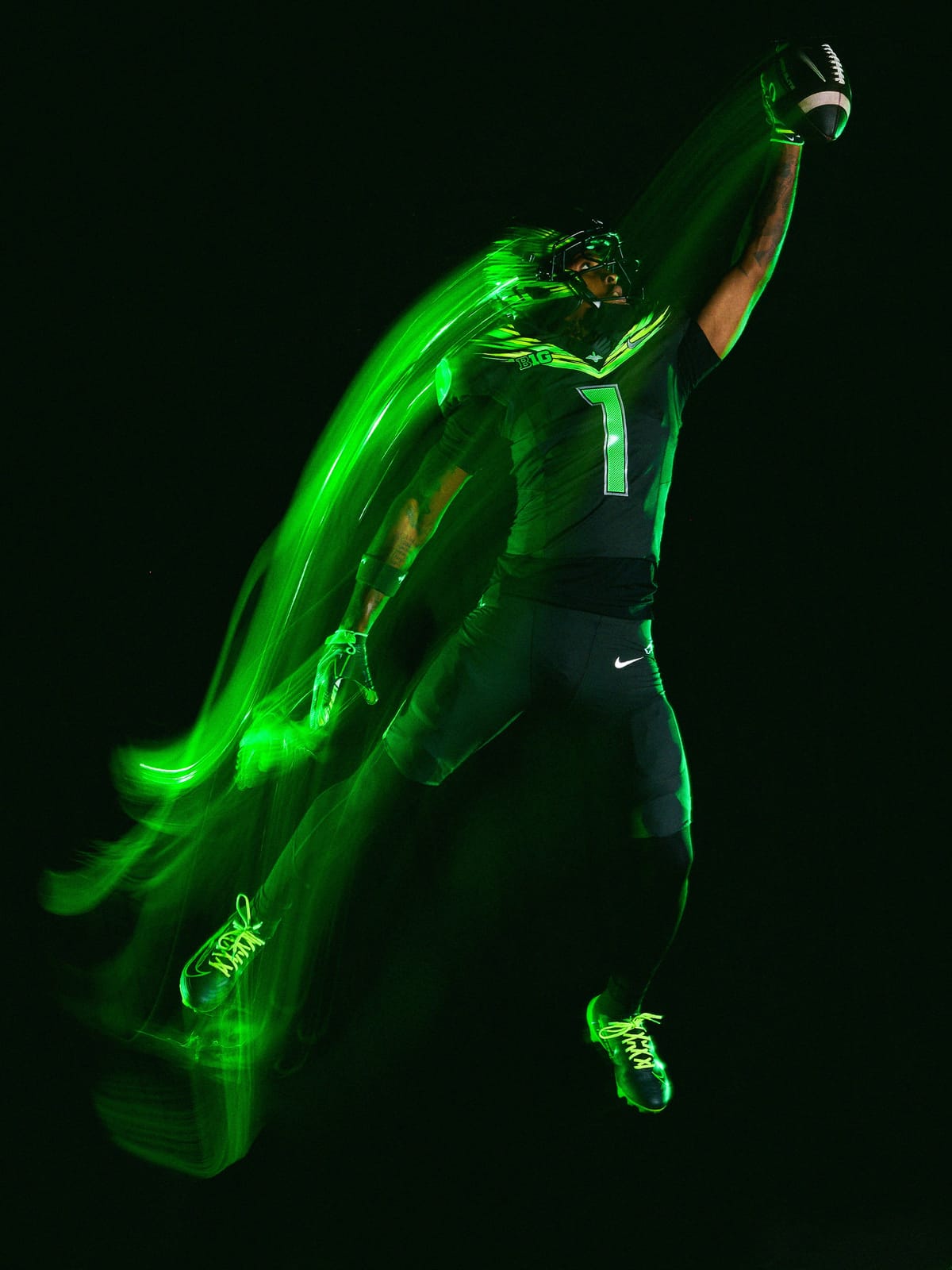 Full-length view of the Oregon Ducks Origin of Speed uniform, dark Night Forest jersey and pants with green streaked shoulder wings, volt cleat laces, shot with green light trails