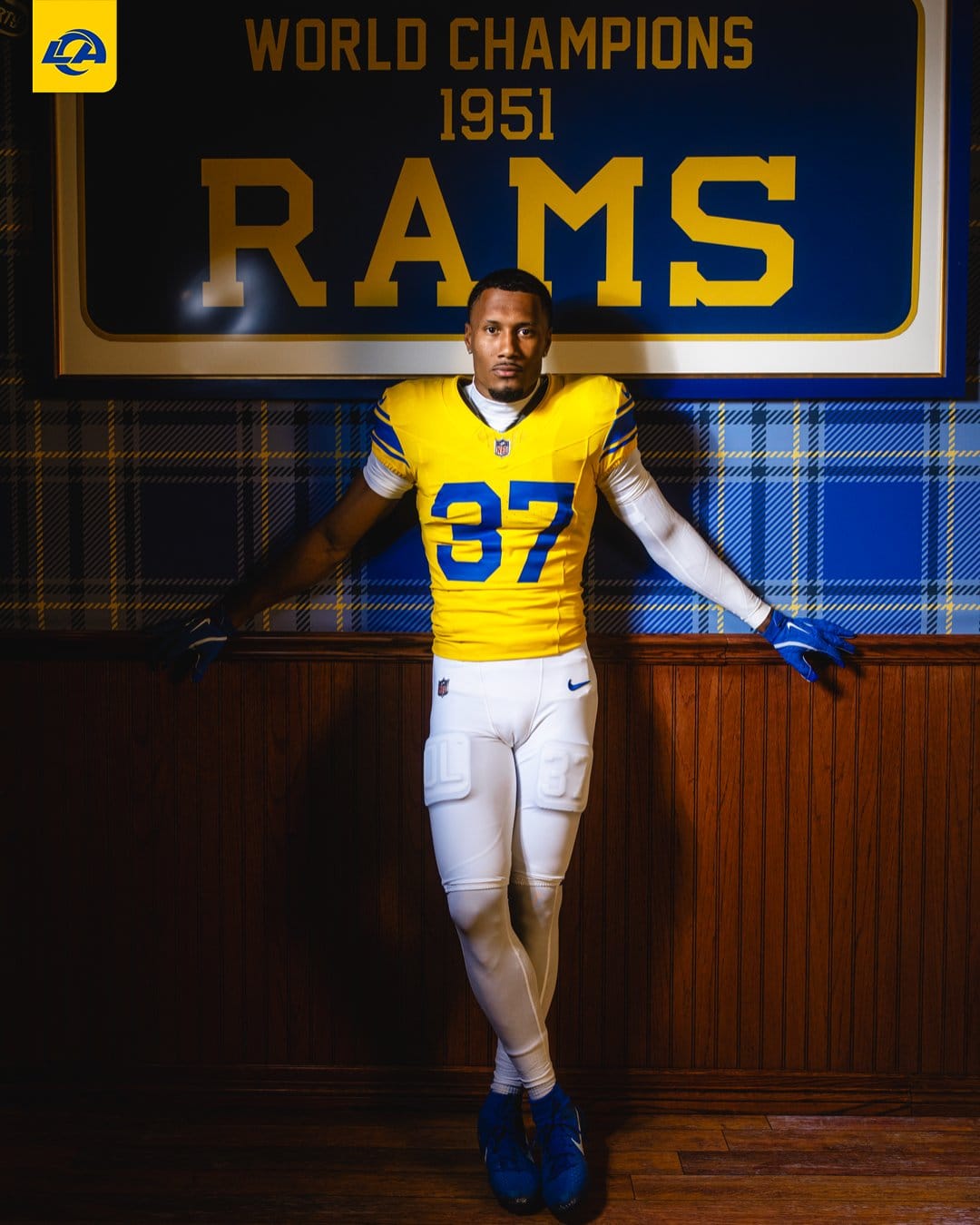 Los Angeles Rams player in the new 2026 Classic Sol gold jersey and white pants in front of a 1951 World Champions Rams banner