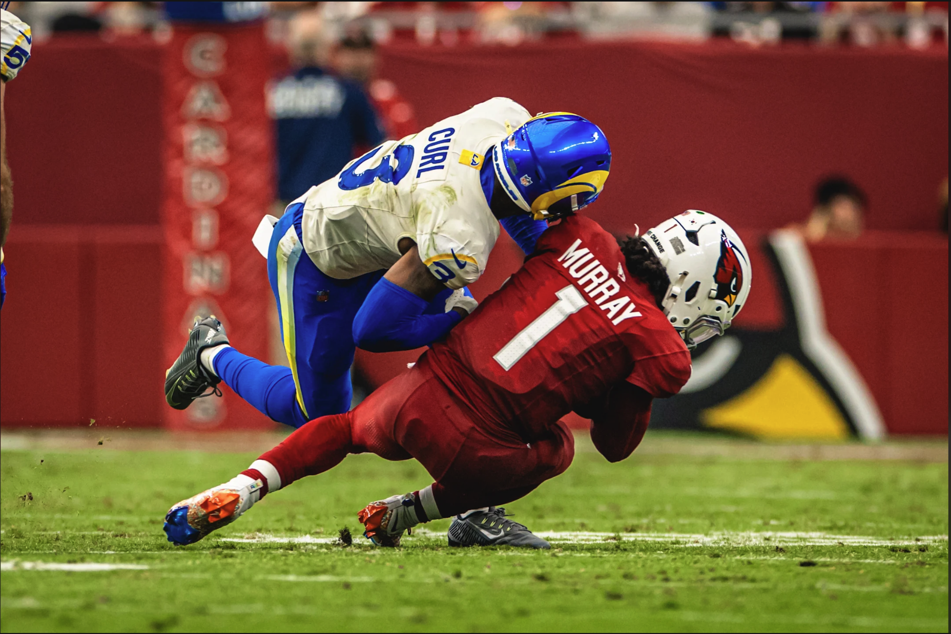 Rams player Curl tackling Cardinals Kyler Murray in bone white away uniform