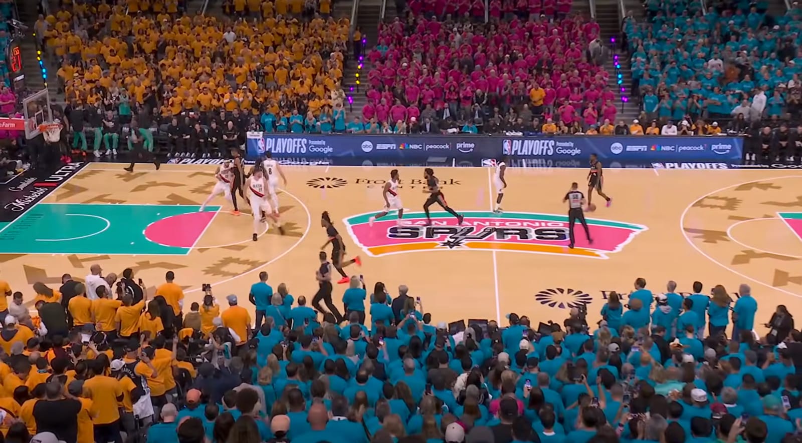 Frost Bank Center wide shot showing full 2026 NBA Playoffs Game 1 Fiesta playoff shirt takeover with teal pink orange and yellow alternating sections and Spurs Fiesta court during San Antonio Spurs vs Portland Trail Blazers
