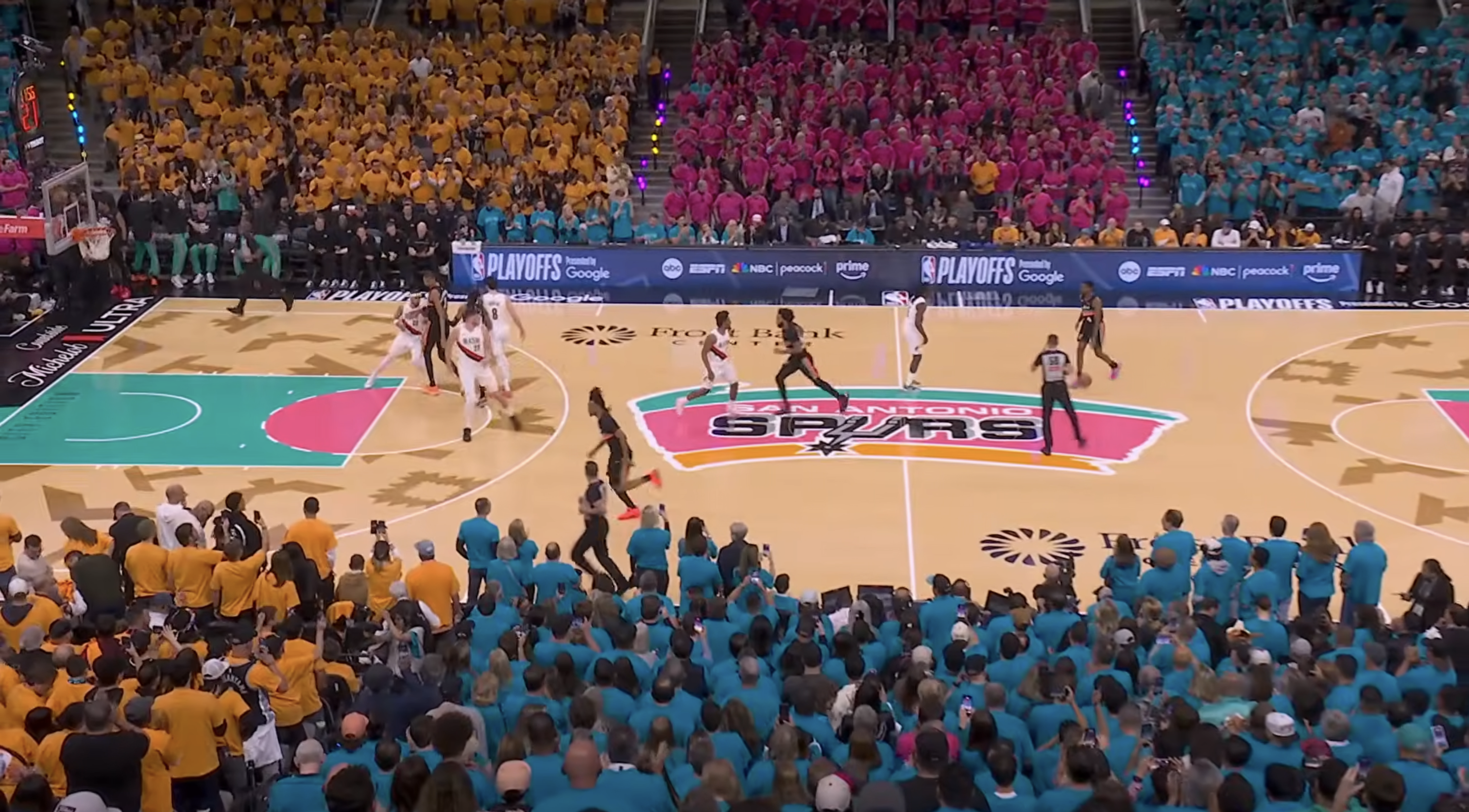 Frost Bank Center wide shot showing full 2026 NBA Playoffs Game 1 Fiesta playoff shirt takeover with teal pink orange and yellow alternating sections and Spurs Fiesta court during San Antonio Spurs vs Portland Trail Blazers