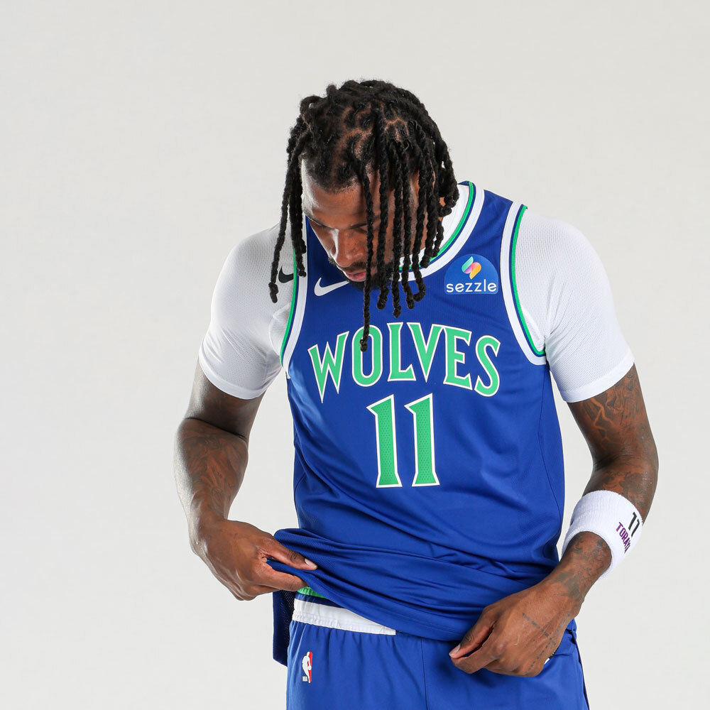 Minnesota Timberwolves new blue road jersey 2026-27 front view with the throwback WOLVES wordmark in green with brighter green outline, Naz Reid #11 in green numerals, brighter saturated blue base from the 1989 expansion identity, and the Sezzle jersey patch on the chest, the primary road uniform for the Wolves 2026-27 NBA season