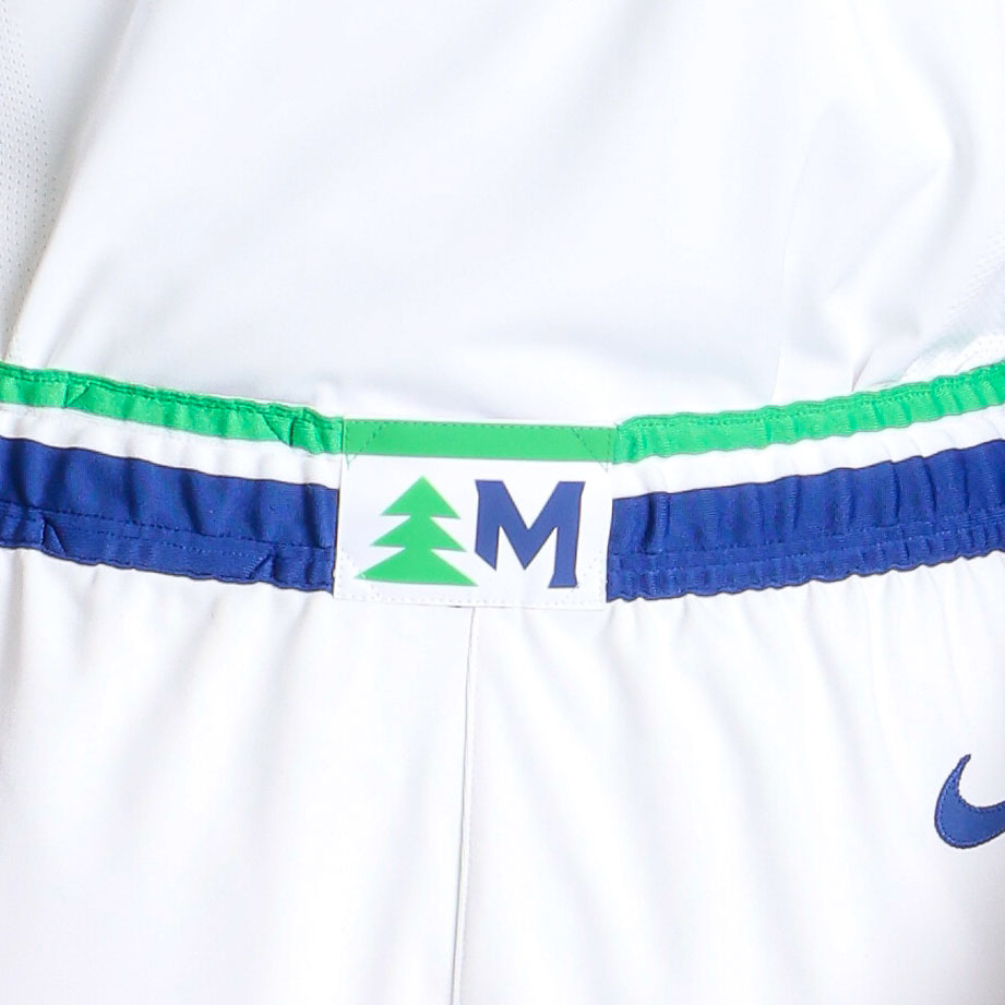 Minnesota Timberwolves new 2026-27 white shorts waistband close-up showing the green tree silhouette and Minnesota M monogram label sitting on a blue base with the green stripe trim, the unifying design element that carries across the white, blue, and black uniform sets of the new Wolves rebrand