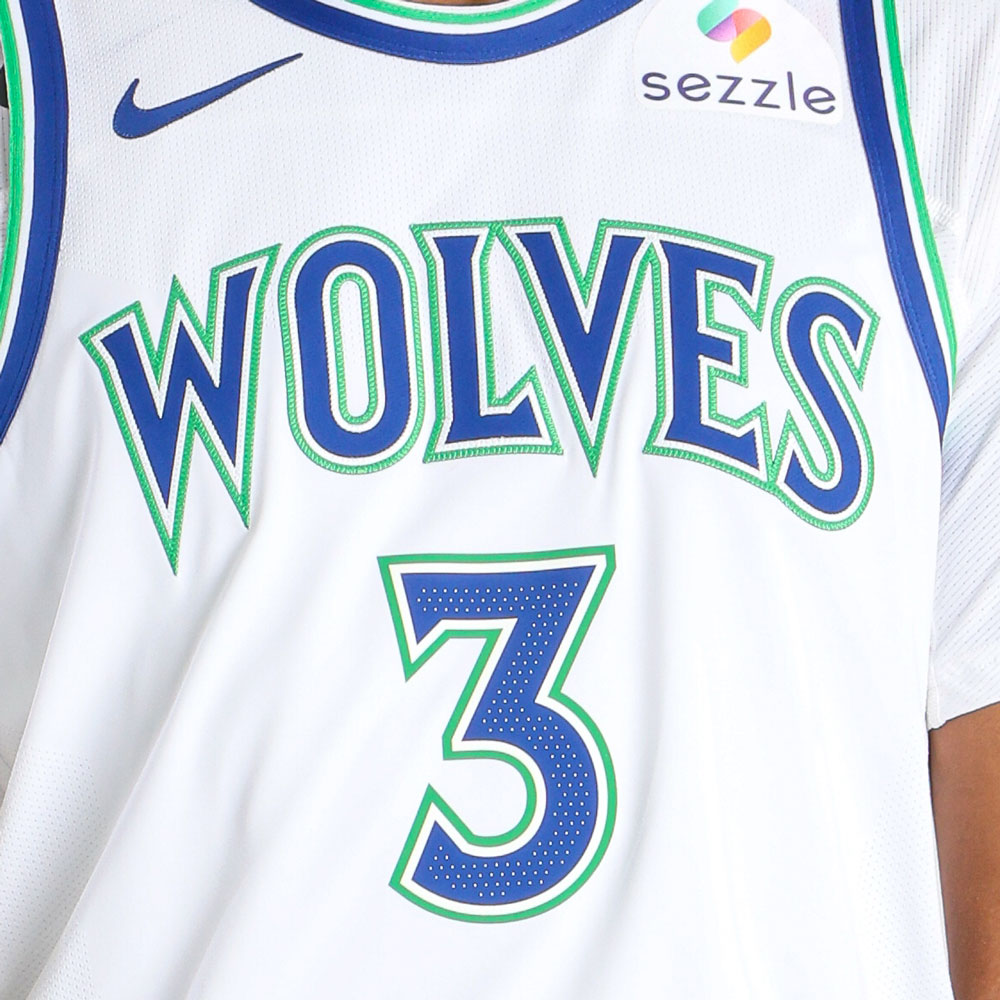 Minnesota Timberwolves new white home jersey 2026-27 WOLVES wordmark and #3 chest close-up showing the embroidered blue letterforms with the bright green outline detail, the Nike swoosh in blue, and the Sezzle jersey patch in full color, the same throwback wordmark treatment from the Kevin Garnett era returning as the new Wolves chest identity