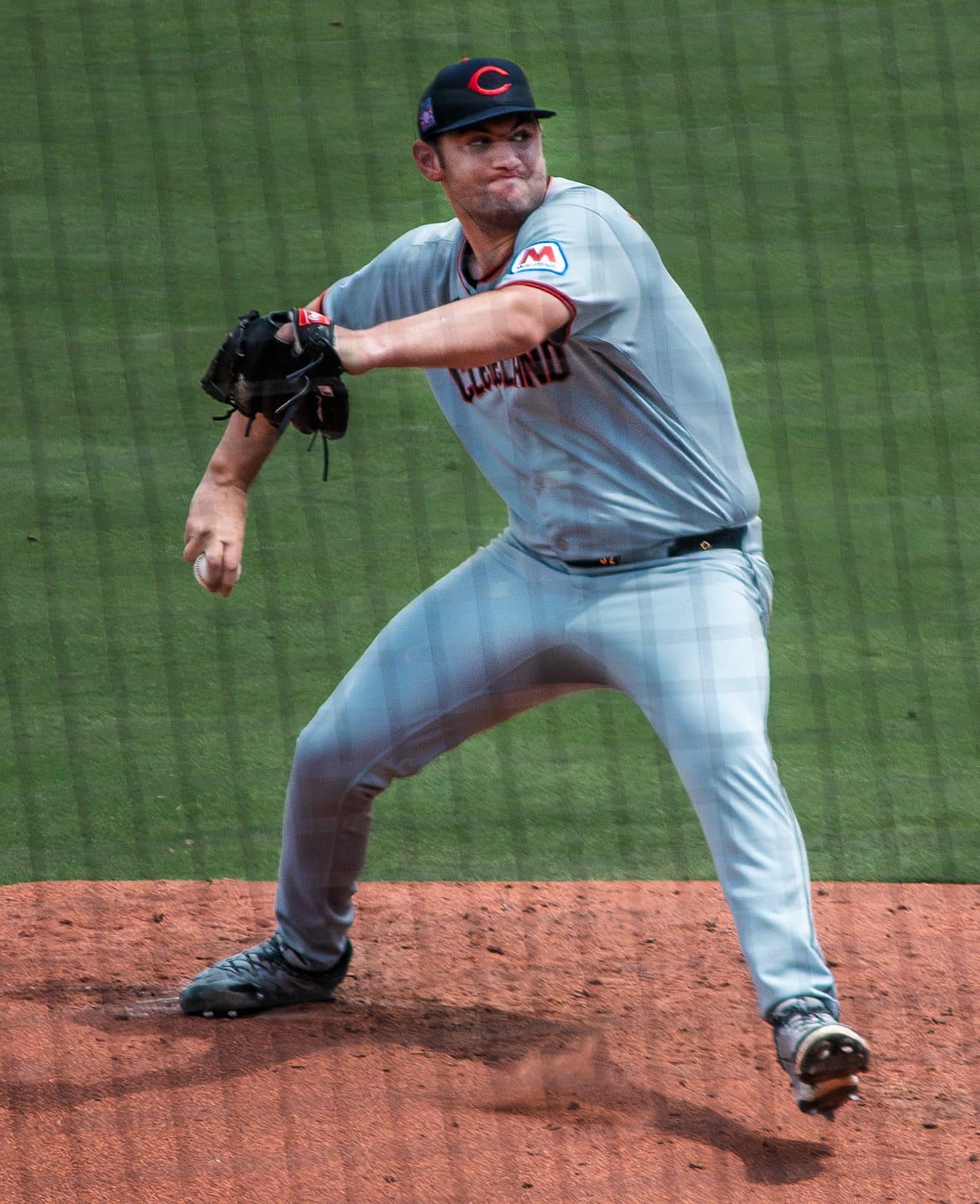 Guardians pitcher Gavin Williams throwing in the gray road uniform with Cleveland across the chest and the navy cap with the red C